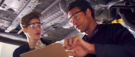 young man and older man standing looking at a clip board in a auto mechanic shop