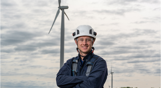 DTE employee wearing safety equipment standing in front of a wind turbine