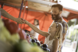 Smiling beard man and his daughter buying groceries on outdoor stand.